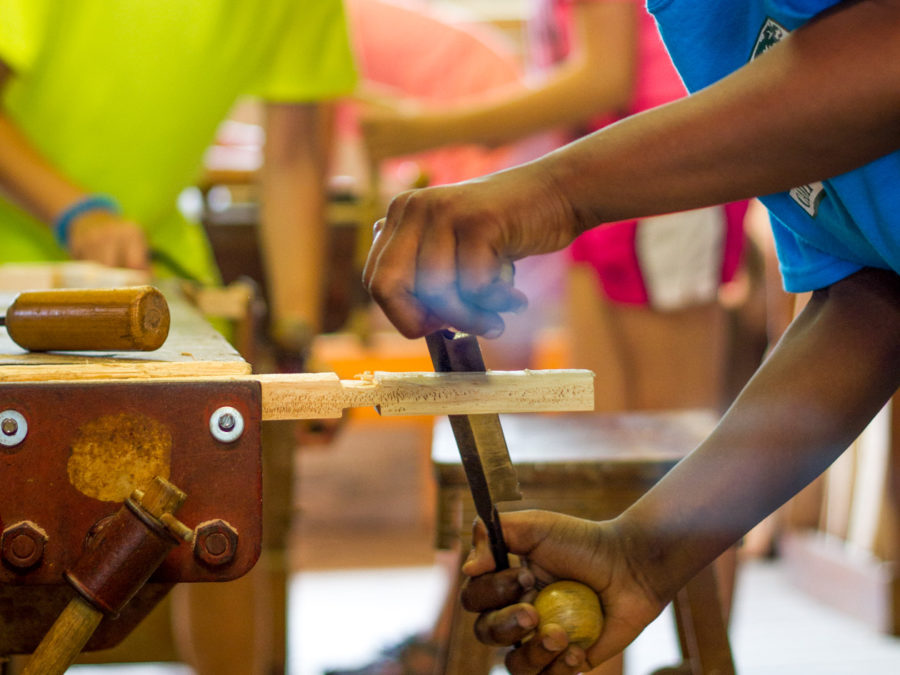 A camper working on a piece of wood in the woodshop.