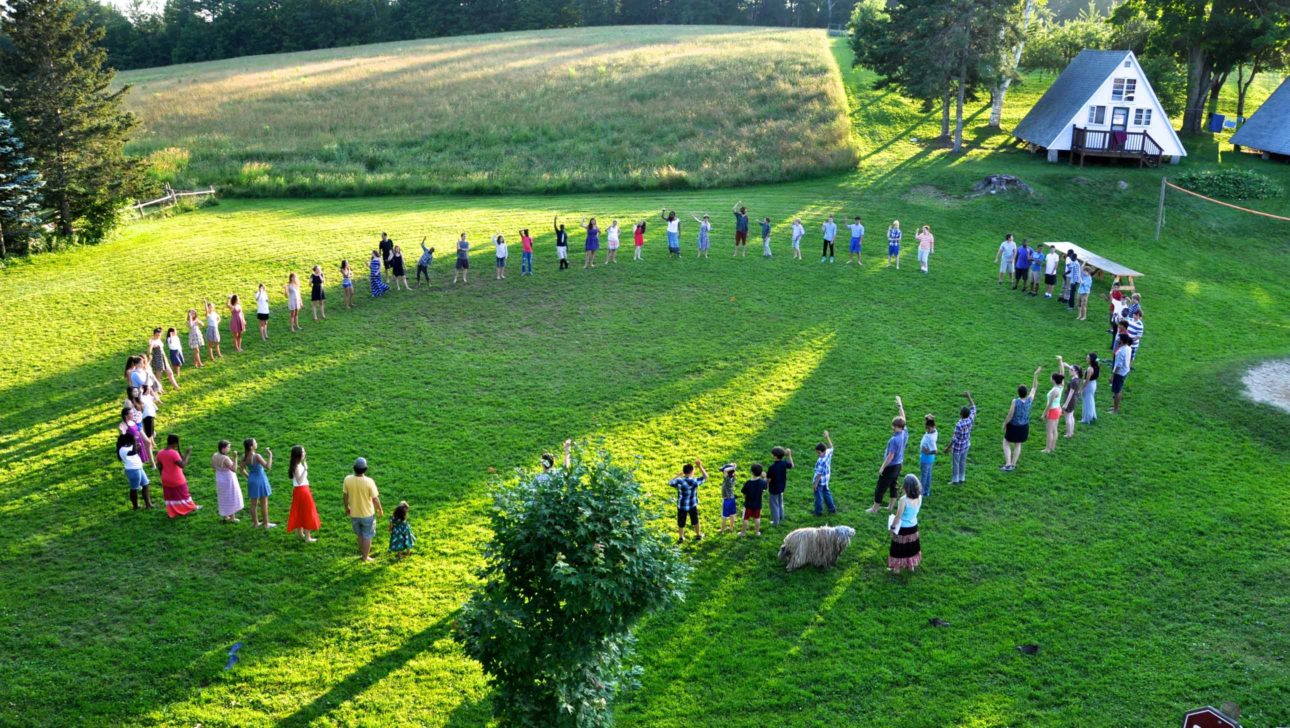 A view of people standing in a circle holding hands in a green field