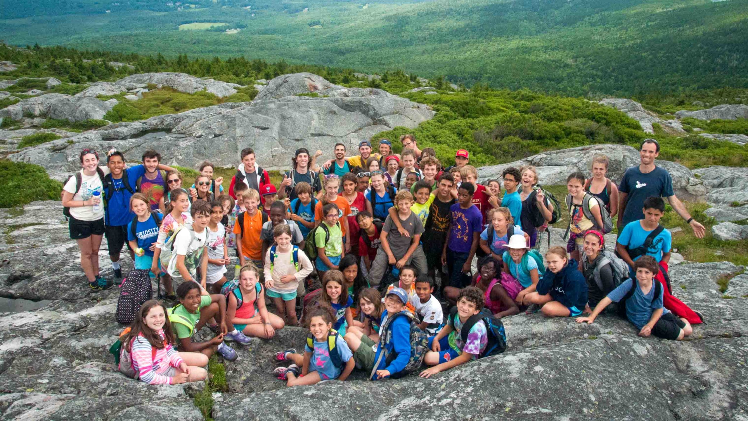 A large group of campers smiling at the camera on a hike on top of a mountain.