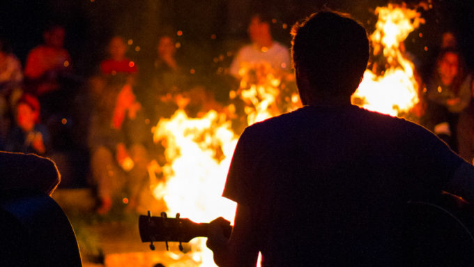 A camper playing the guitar at the camp fire.