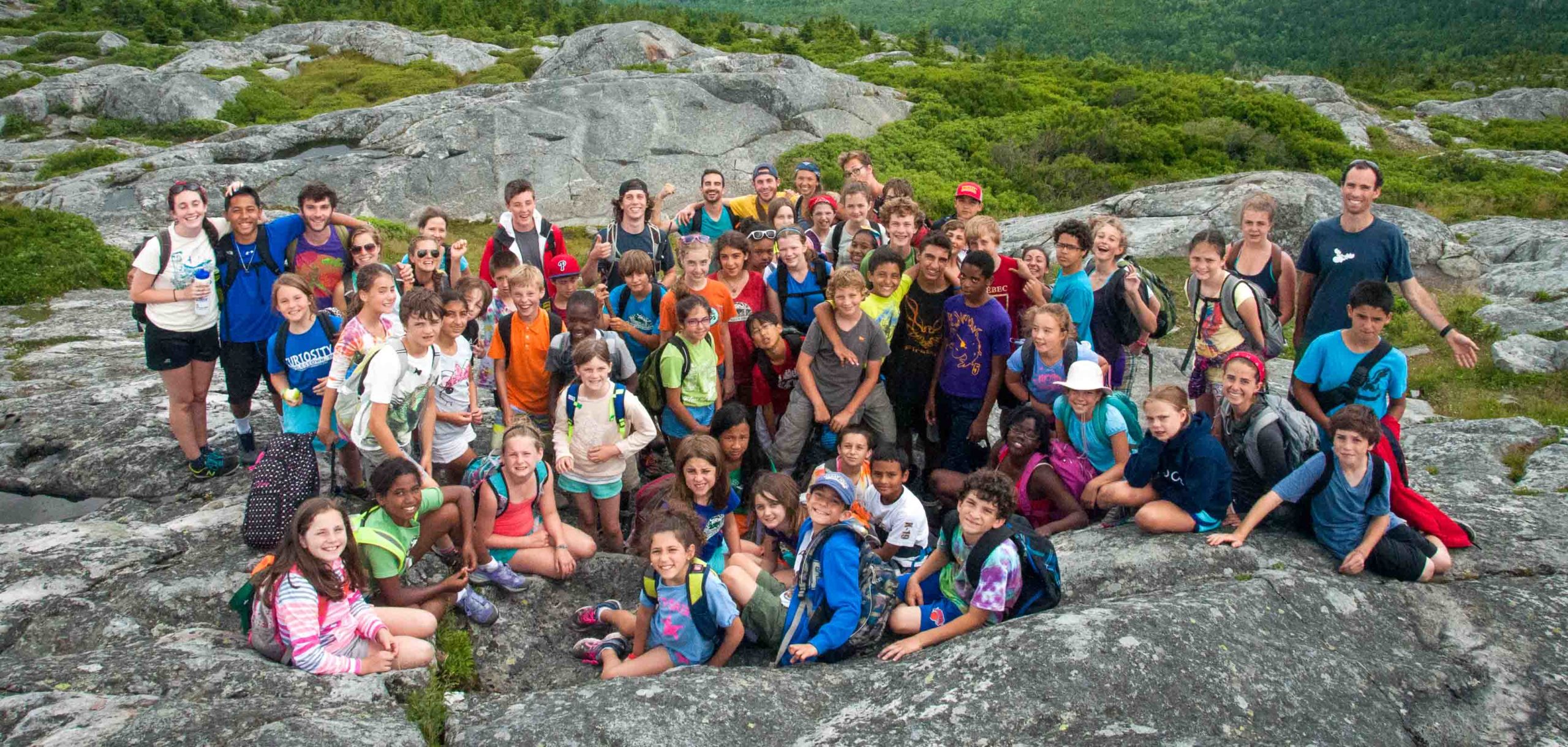 A large group of campers smiling at the camera on a hike on top of a mountain.