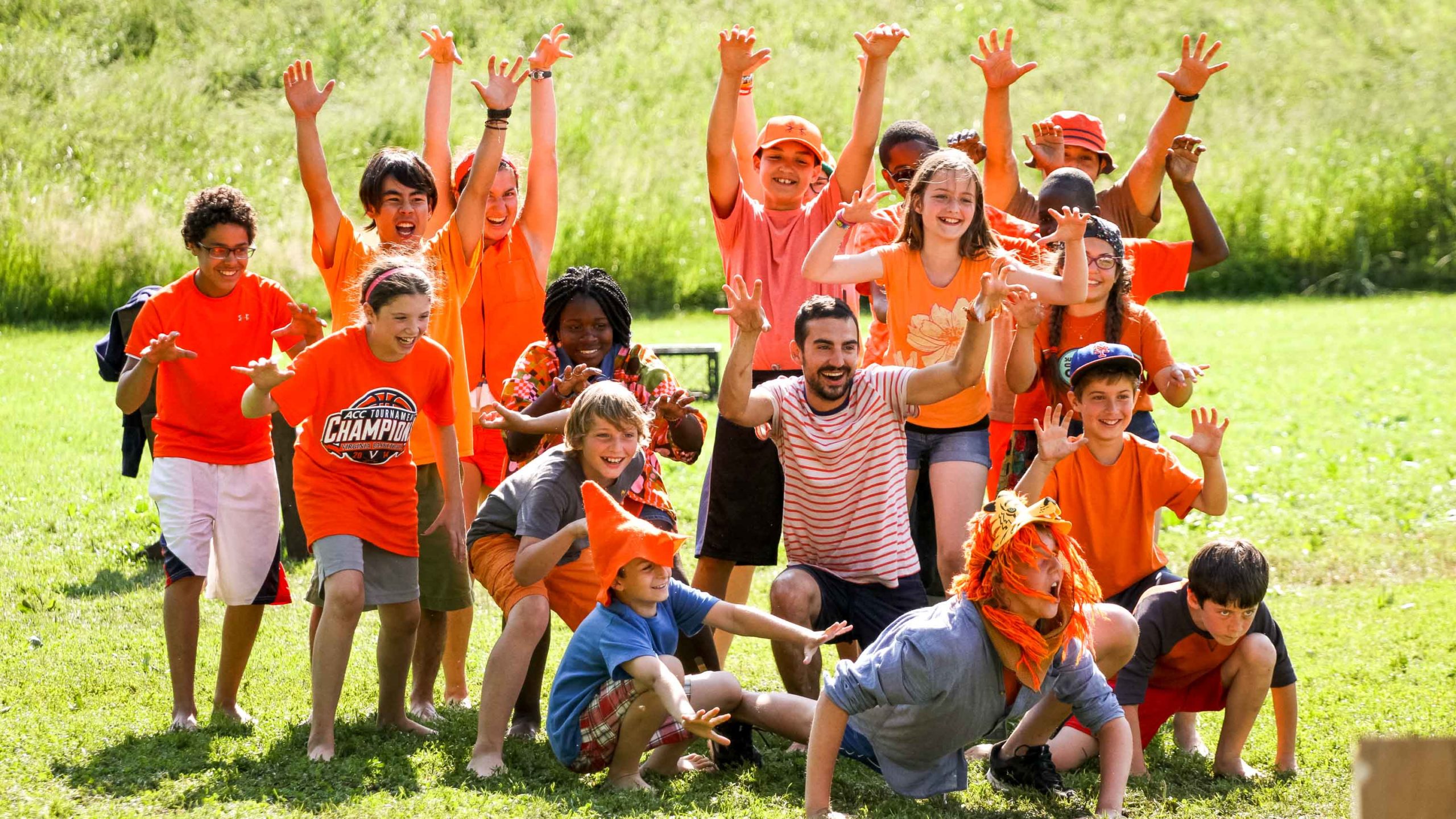 A group of campers posing wearing orange with their hands up.