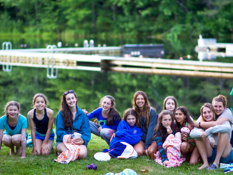 A group of campers sitting in front of the lake smiling.