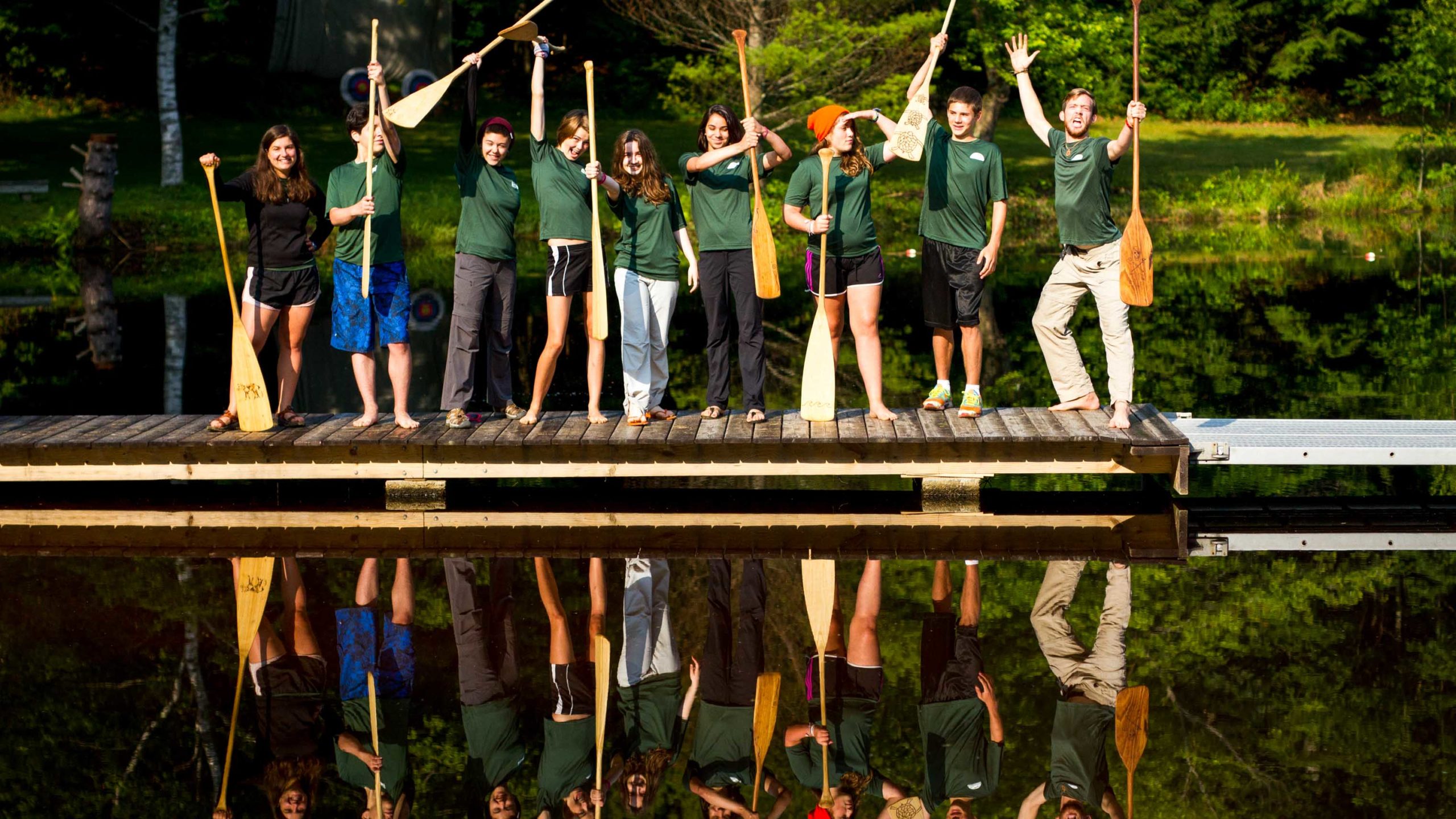 Campers standing on the dock holding paddles in the air.