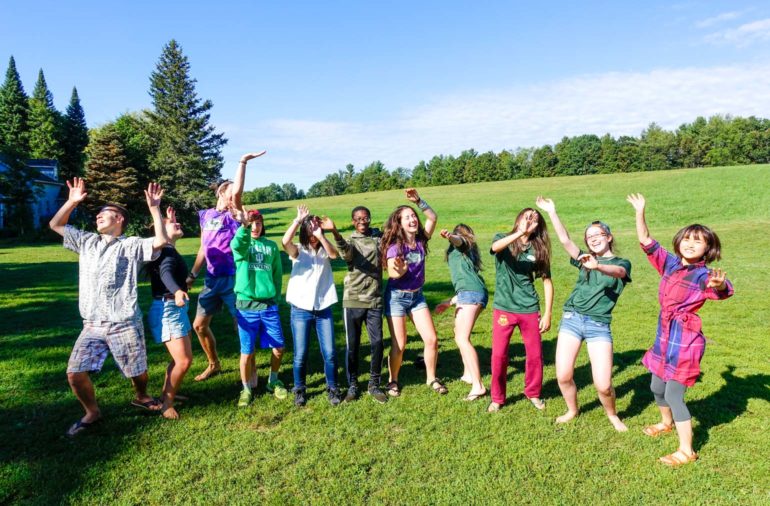 Campers dancing and posing for the camera in a green field.