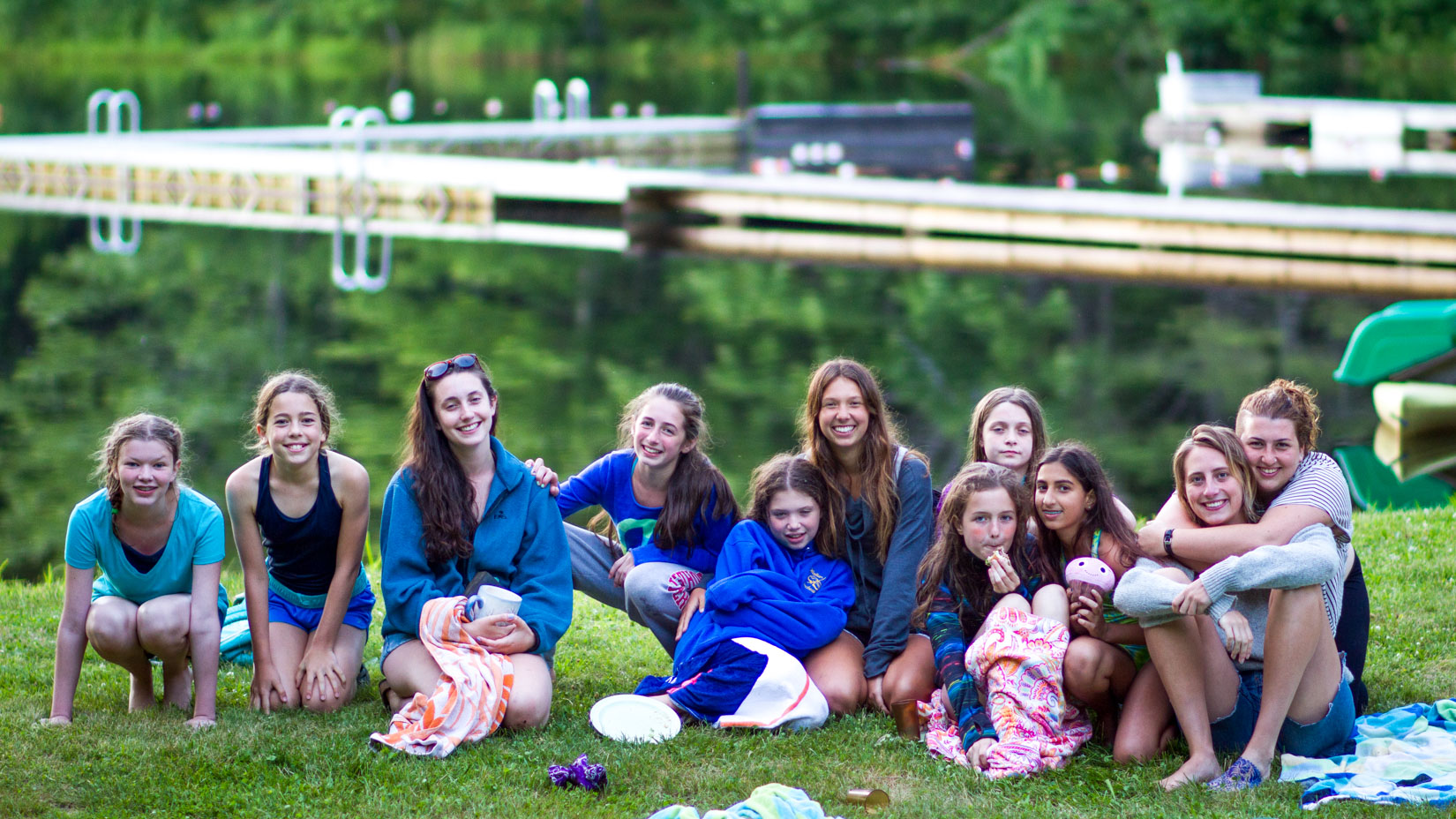 A group of campers sitting in front of the lake smiling.