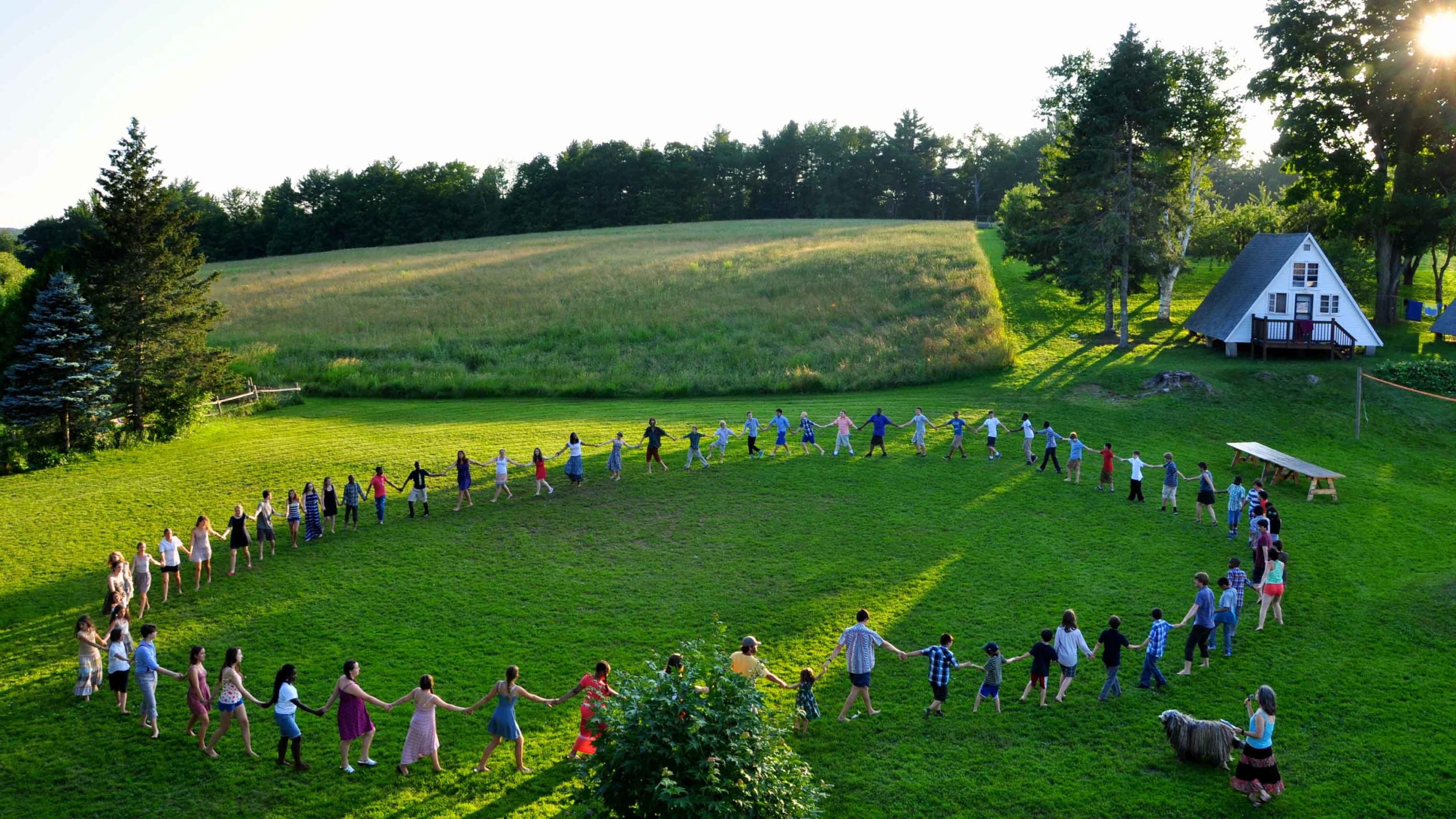 A view of people standing in a circle holding hands in a green field
