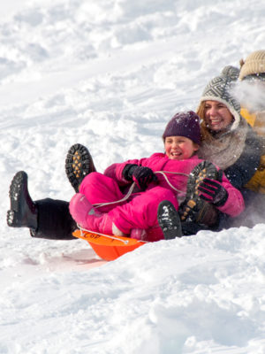 Campers laughing while sledding down a hill.